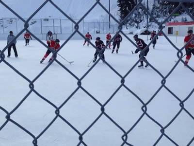Chain link fence around ice hockey field, and two teams are fighting fierce.