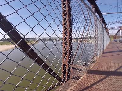 A metal bridge with chain link railing across a deep and wide river.