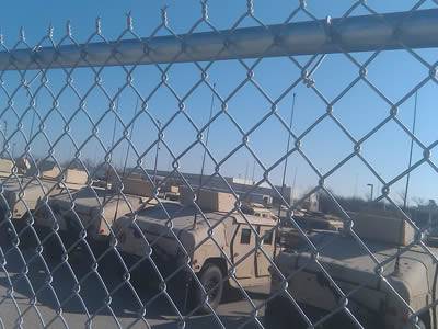 Chain link fence around military camp, and a row of orderly tanks behind the fence.