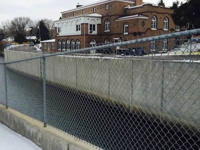 A river channel with chain link security fence, in front of a department.