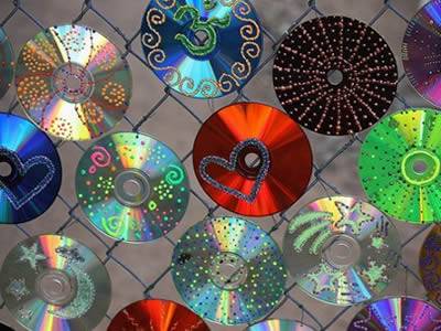 Colorful CDs hanging on blue chain link fence.