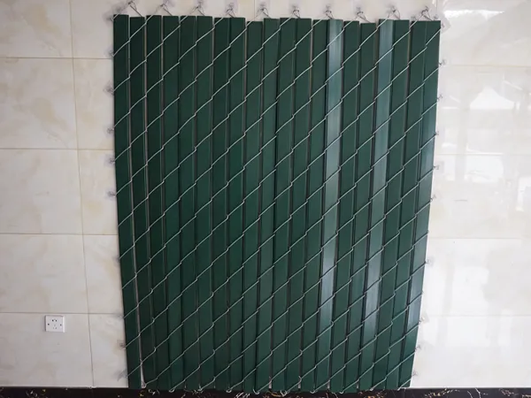 Green chain link fence slats are hanging on a wall for display.