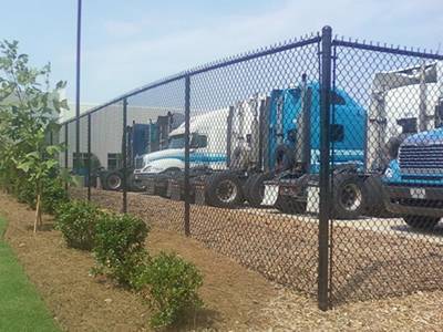 A black commercial chain link fence in front of many trucks.
