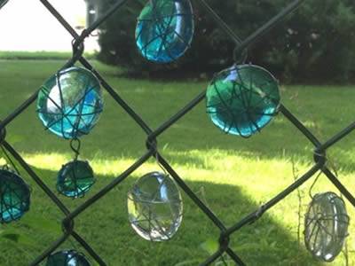 Green and white glass balls hanging on chain link fence by thin wires.