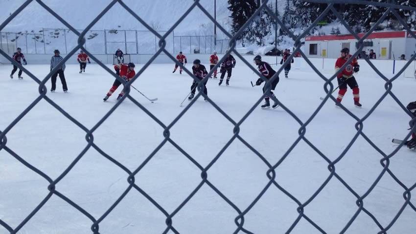 Chain link fence around ice hockey field, and two teams are fighting fierce.