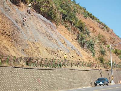 Chain link fence covers the bare slope in the mountain side of the highway.