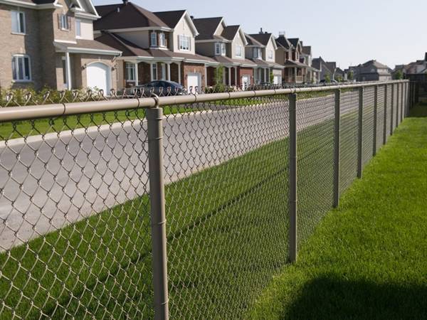 The aluminum coated chain link fencing is installed along the roadside of residences.