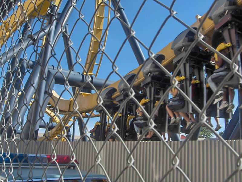Chain link fence on the side of roller coaster, and people are on roller coaster's seats.